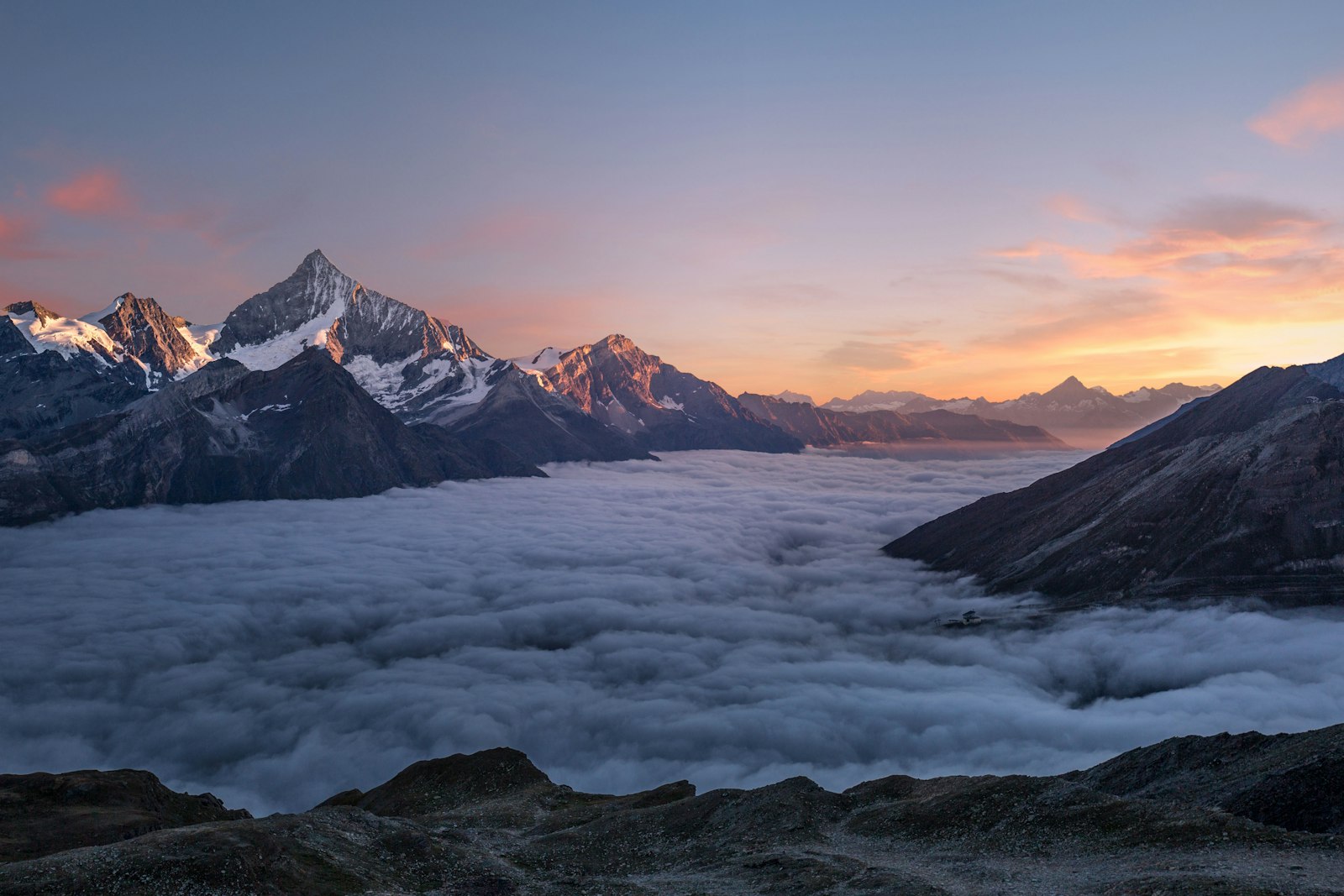 Snow peaks standing above a sea of cloud at sunset