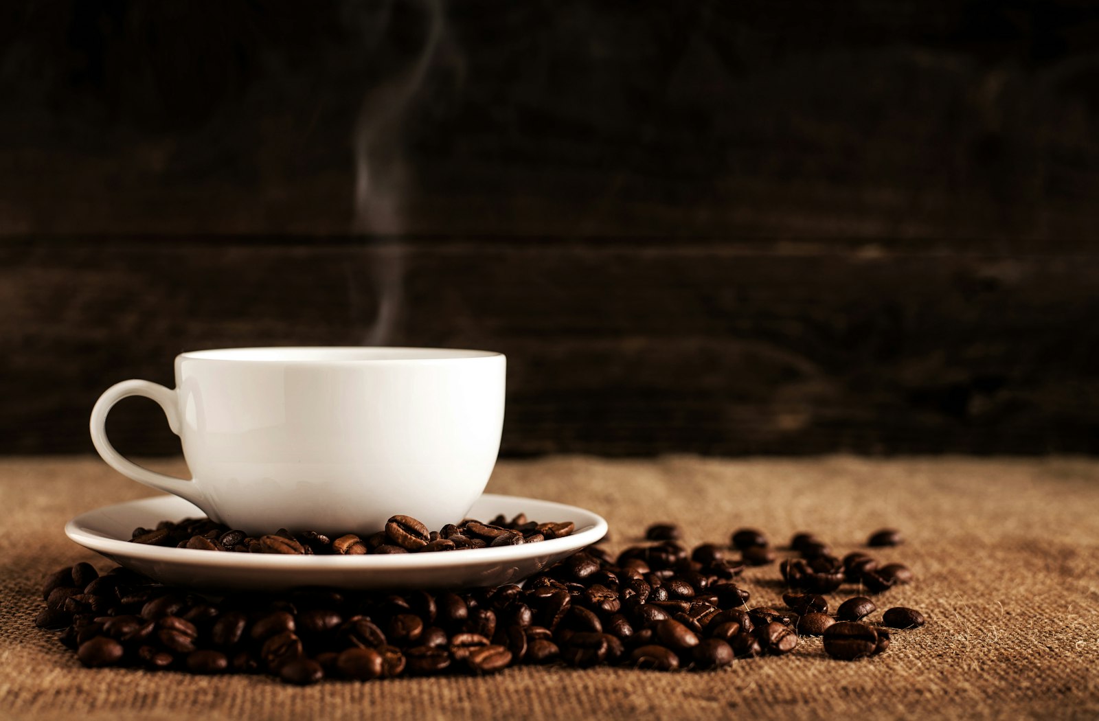 A steaming white cup of coffee on a bed of roasted beans
