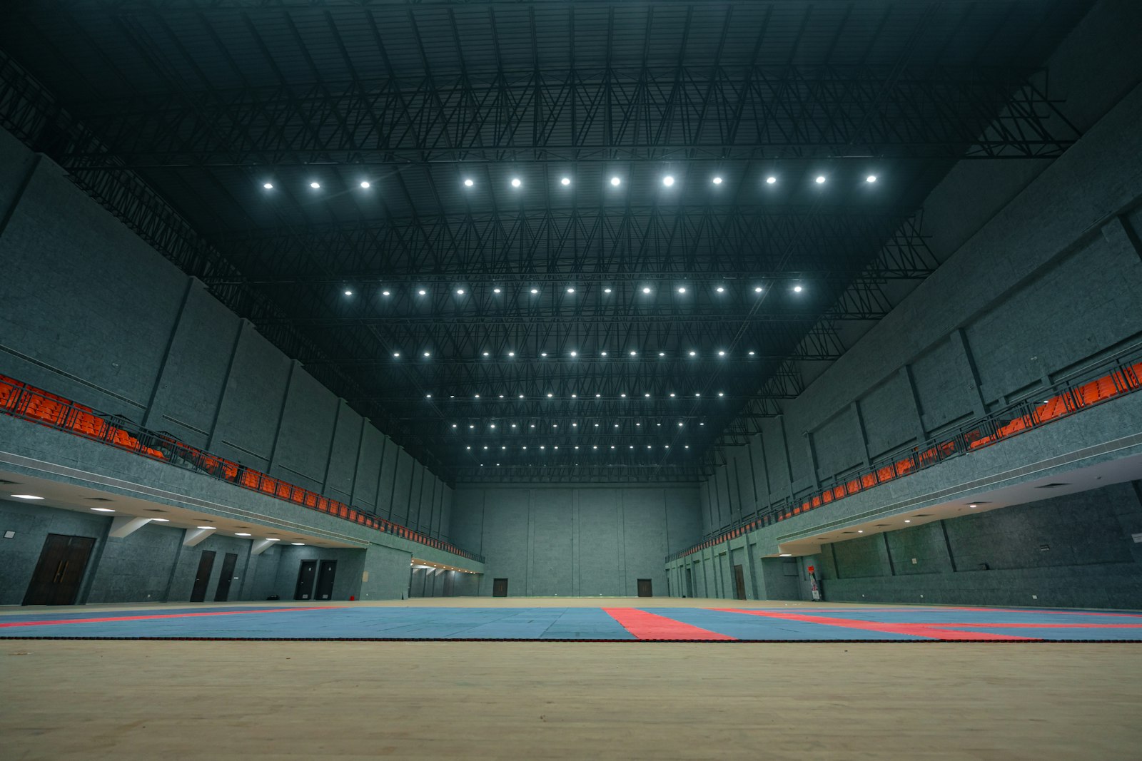 A wide training hall with blue and red mats under bright ceiling lights